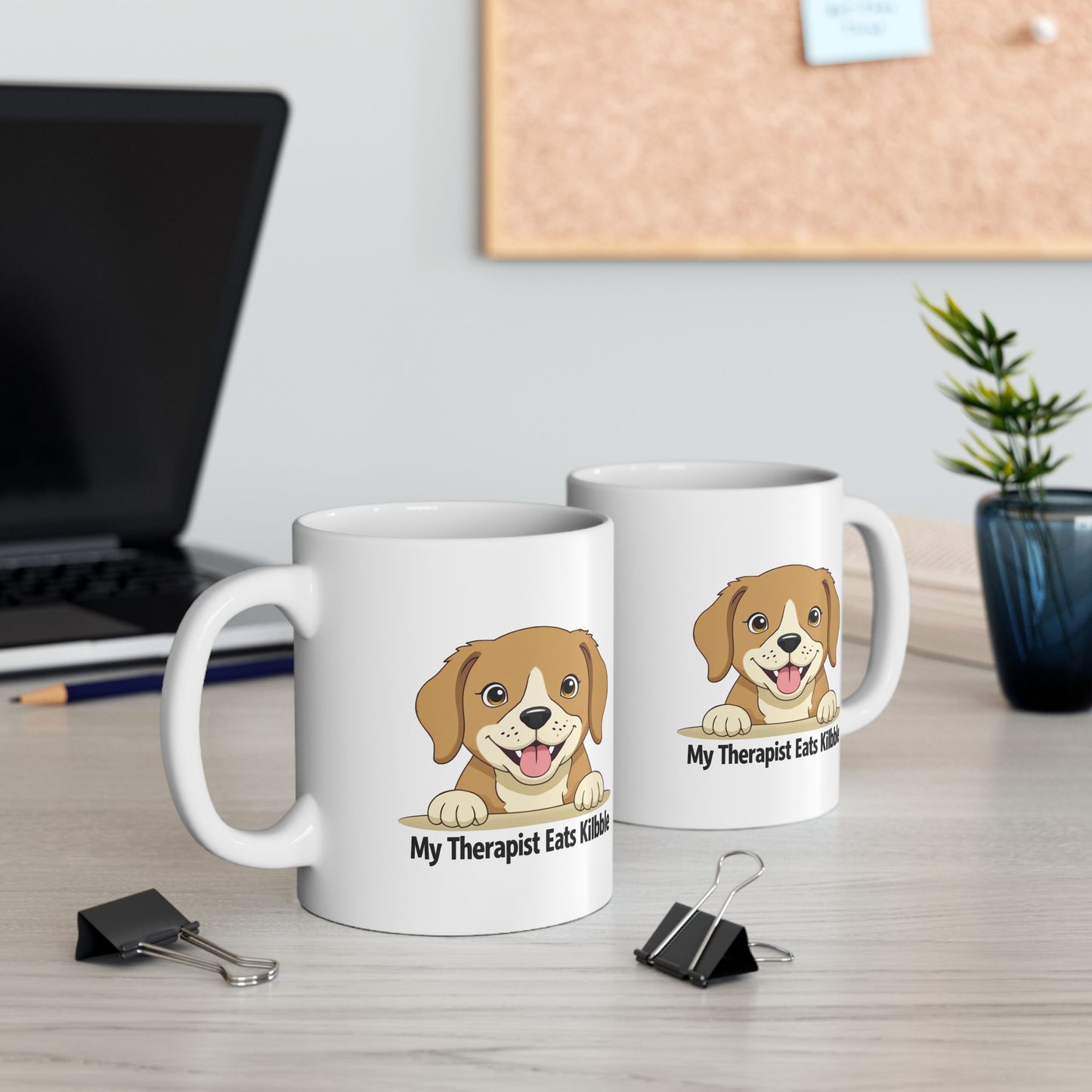 Two white mugs with a dog illustration and text on a desk.