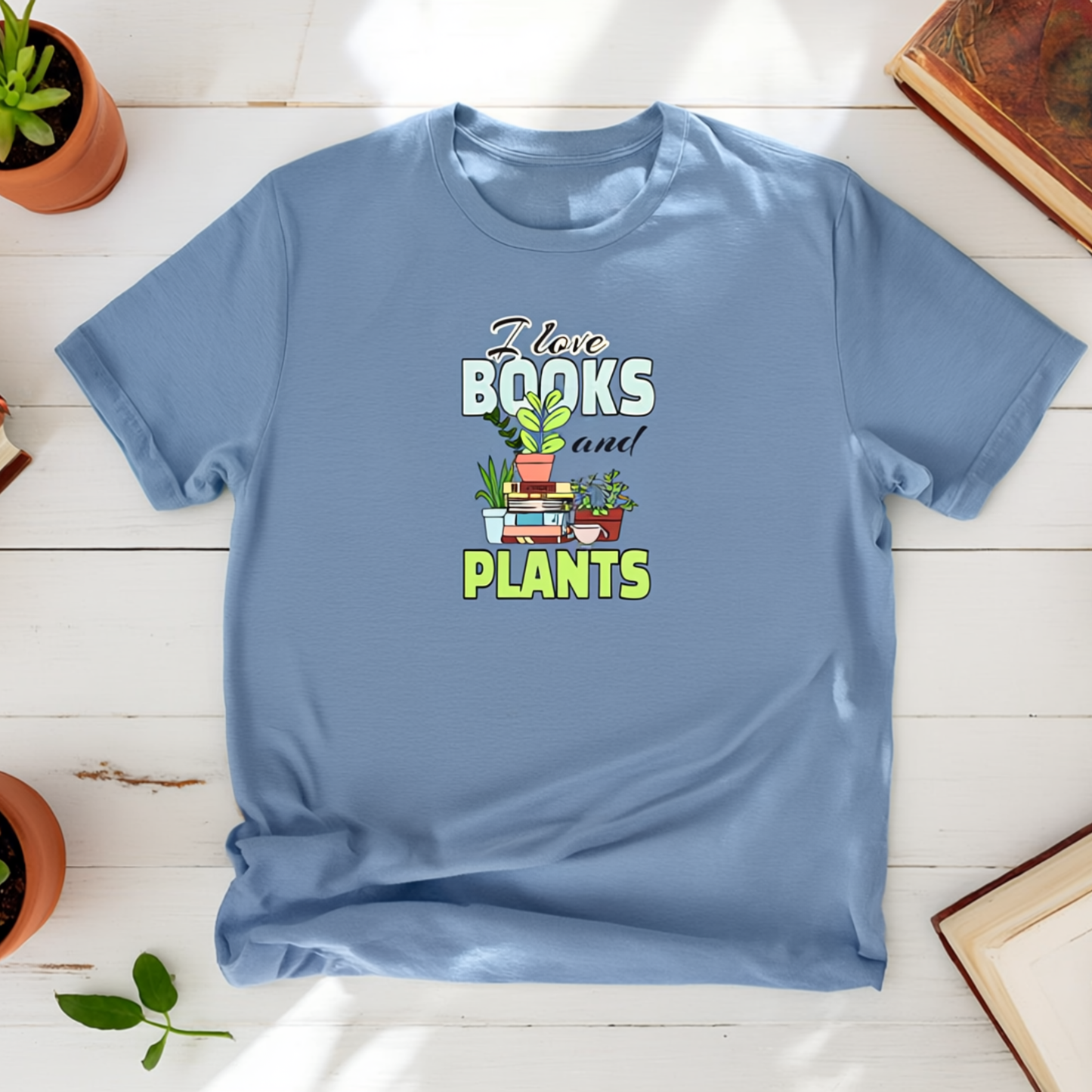 Blue t-shirt with 'I love books and plants' design on a wooden surface with potted plants.